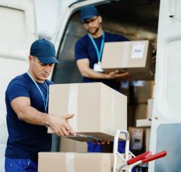 young-courier-his-colleague-unloading-cardboard-boxes-from-delivery-van (1)